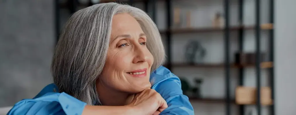 An older woman sitting indoors with her arms folded
