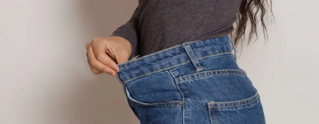 A person holding out the loose waistband of their jeans